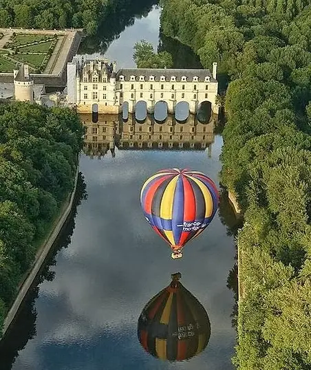 Aerial view of Château de Chenonceau spanning the River Cher with a colorful hot air balloon and its reflection, Loire Valley France