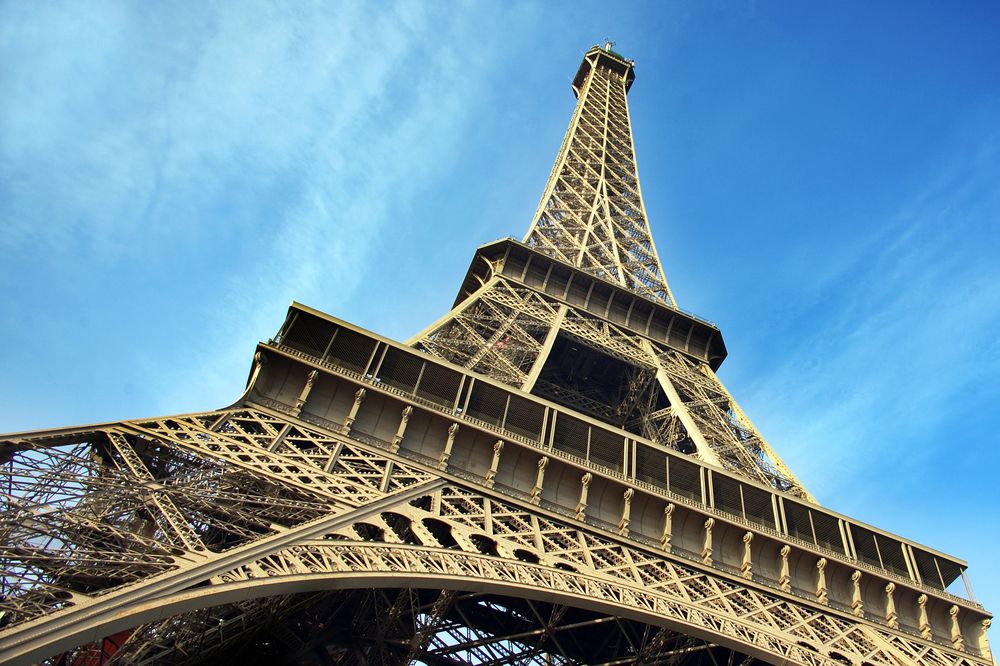 Looking up at the Eiffel Tower iron lattice structure against a blue sky on a luxury Paris tour, France