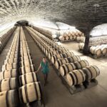Stephanie Burtin walking through vast Burgundy Grand Cru cellar with hundreds of oak barrels in vaulted stone tunnels on a luxury wine tour, France