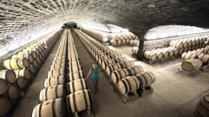 Stephanie Burtin walking through vast Burgundy Grand Cru cellar with hundreds of oak barrels in vaulted stone tunnels on a luxury wine tour, France