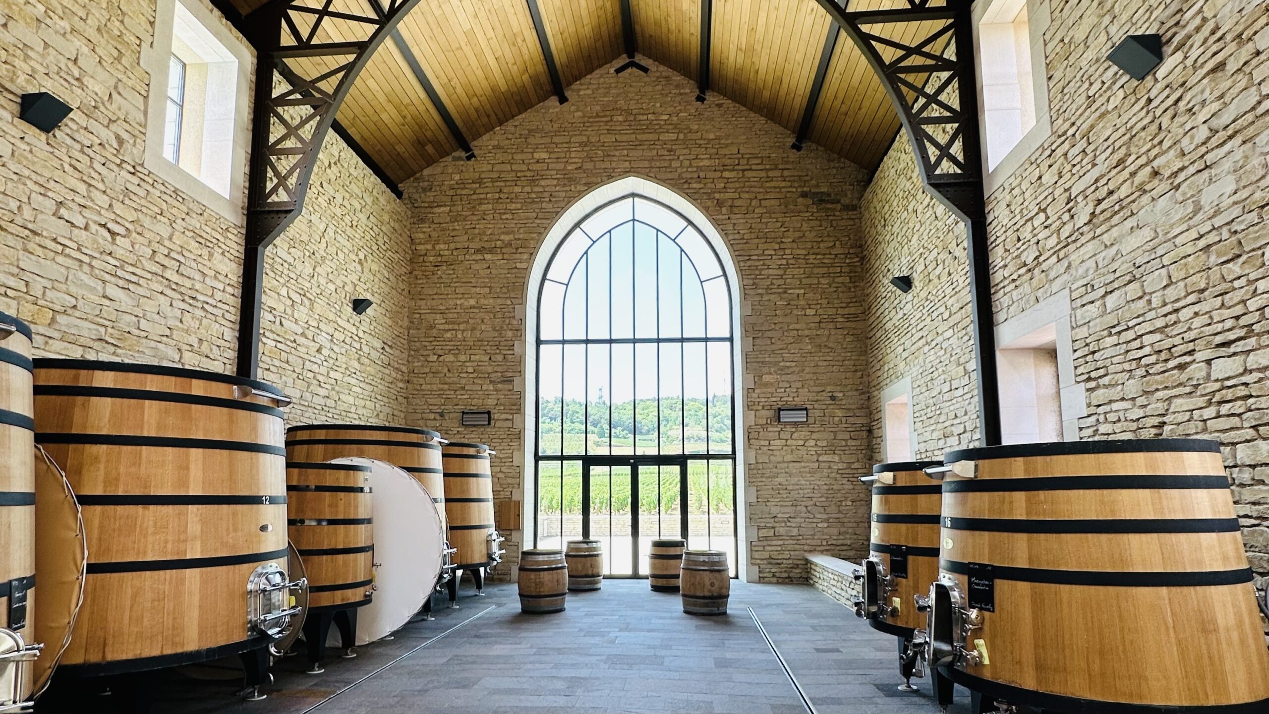 Modern Burgundy winery with large oak fermentation vats and Gothic arched window overlooking vineyards on a luxury wine tour, France