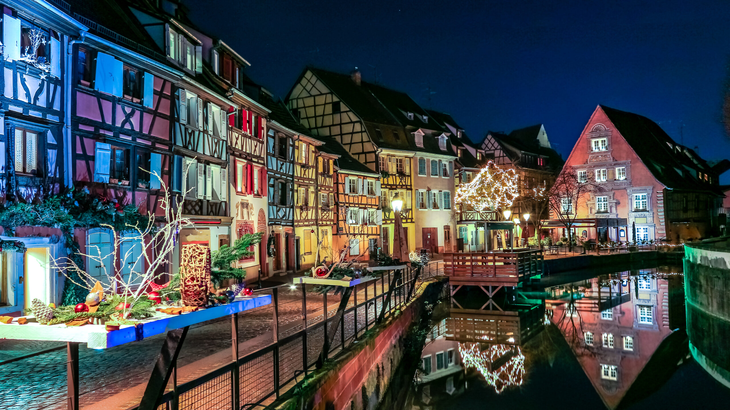 Colmar Christmas market canal at night with colourful illuminated half-timbered houses and festive decorations reflected in water, Alsace, France