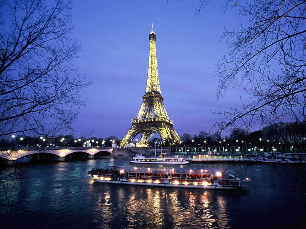 Eiffel Tower illuminated at night above the Seine River with a dinner cruise boat on a luxury Paris tour, France