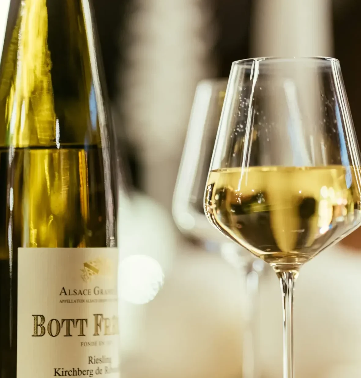 Bott Frères Alsace Grand Cru Riesling Kirchberg bottle and white wine glass at a fine dining table, Alsace, France