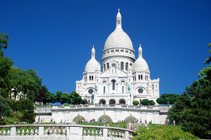 Sacré-Cœur Basilica white domes rising above Montmartre hill gardens under a deep blue sky, Paris, France
