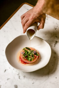 Chef pouring sauce over an elegant tomato and edible flower dish at Saint James Paris Michelin star restaurant, France
